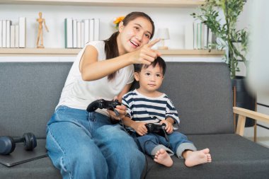 Bir anne ve küçük oğlu kanepede eğlenceli bir oyun oynuyorlar, aile bağlarını ve oyuncu etkileşimlerini vurguluyorlar..