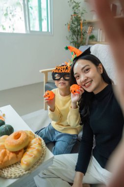 Neşeli bir anne ve oğul birlikte poz verir, Cadılar Bayramı süslerini ve hediyelerini sergiler, bayram mevsimini kutlarlar..