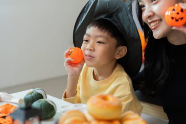 Cadı şapkalı bir çocuk annesiyle Cadılar Bayramı şenliklerinin tadını çıkarıyor. Etrafı şen şakrak süslerle çevrili..