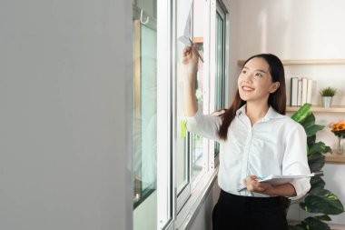 Profesyonel bir kadın görevlerini yönetirken pencere dekorasyonunu ayarlar, olumlu bir çalışma ortamı oluşturur.