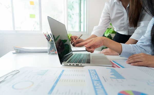 Women pointing at laptop screen while analyzing data, showcasing teamwork and focus on financial metrics in a bright office environment.