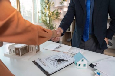 Bir alıcı ve emlakçı, modern ofis ortamında başarılı bir anlaşmayı kutlamak için sözleşmeyi el sıkışır..