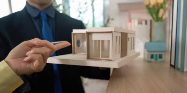 Bir emlakçı, modern ofis ortamında özellikleri ve düzeni tartışan bir müşteriye ev modelini vurgular.