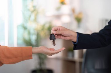 Bir emlakçı, emlak alımının başarıyla tamamlanması için anahtarlarını bir müşteriye teslim eder..