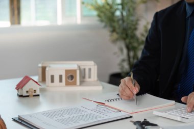 Bir emlakçı, istişare sırasında mülkiyet belgelerini ve notlarını inceleyerek profesyonellik ve ayrıntılara dikkat çeker..