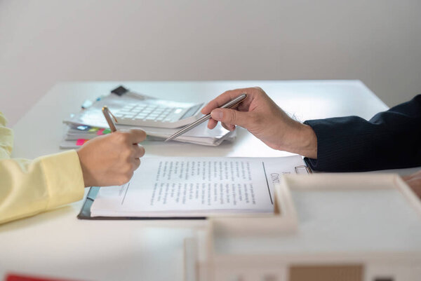 A client and agent engage in a business negotiation, exchanging pens and discussing contract details at a modern office table.