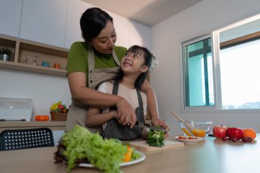 Bir anne ve kızı, birlikte sebze doğrarken, parlak bir mutfakta yemek pişirme sevgisi beslerken mutlu bir anı paylaşıyorlar..