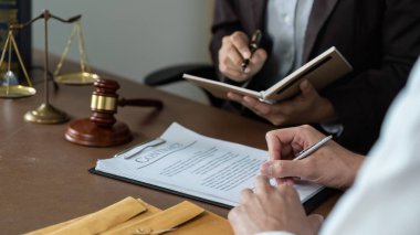 Bir avukat, müvekkilinin sözleşmesini gözden geçirir, notlar alır ve profesyonel bir ortamda tüm detayların anlaşılmasını sağlar..