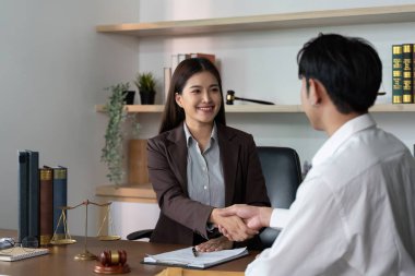 Bir avukat ve müvekkil el sıkışır, anlaşmanın sembolü ve hukuki danışma ayarına güvenir.