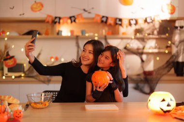 Bir anne ve kızı oyulmuş bir balkabağıyla selfie çekip Cadılar Bayramı 'nı gülümseme ve kahkahalarla kutluyorlar. Bir neşe ve bağlantı anı.