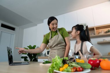 Neşeli bir anne kızına modern bir mutfakta sağlıklı yemek pişirmeyi öğretir. Aile bağlarını ve beslenmeyi teşvik eder..