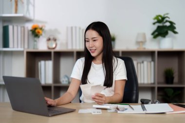 Genç bir kadın, mali durumunu dizüstü bilgisayarla yönetirken gülümsüyor ve finansal güçlenmeye olumlu bir yaklaşım sergiliyor..