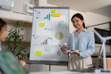 Profesyonel bir kadın, çağdaş bir çalışma alanında sunum sırasında ESG ölçümleri ve sürdürülebilirlik stratejilerini tartışır.