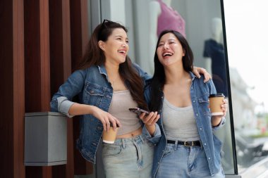 İki arkadaş keyifli bir anı paylaşıyor. Çağdaş bir binanın dışında kahve içip gülüyorlar. Arkadaşlığımızı kutluyorlar..