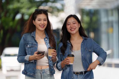 Dışarıda yürürken gülümseyen ve kahve fincanı tutan iki genç kadın, dostluğu ve bağlantıyı kutluyorlar. Yaşam tarzı temaları için mükemmel.