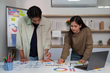 İki tasarımcı ortak bir UX UI tasarım oturumuna katıldı, fikir üretme ve tasarım malzemeleriyle dolu bir masada çizim yapma.