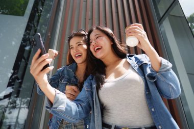 İki neşeli kadın ellerinde kahve fincanlarıyla gülüyor ve şehrin güneşli gününün tadını çıkarıyorlar..