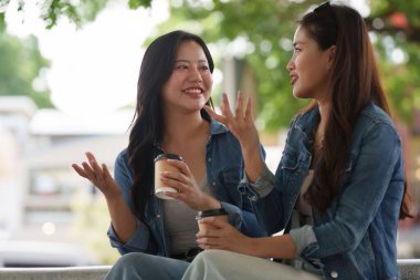 İki genç kadın, canlı bir açık hava ortamında, arkadaşlığımızı kutlamak için kahve içerken keyifli bir sohbet ediyorlar..