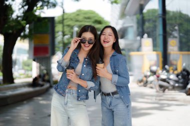 İki arkadaş açık havada keyifli bir anı paylaşıyor, ellerinde kahve fincanları ve gülümsüyor, canlı bir şehir yaşam tarzı sergiliyorlar..