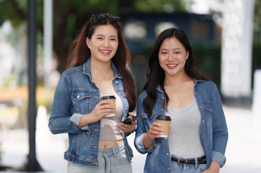 İki arkadaş kahkaha ve kahveyi açık havada paylaşıyor. Arkadaşlığın ve bağlantının neşesini vurguluyorlar..