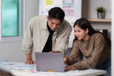 Modern bir çalışma alanında, takım çalışması ve yaratıcılığı sergileyen bir dizüstü bilgisayar üzerinde ortak bir tartışmaya giren iki genç profesyonel..