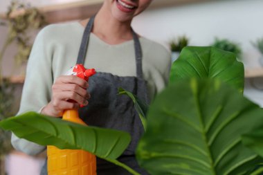 Bir kadın yemyeşil çiçeklerine su sıkarken gülümsüyor. Kapalı bir ortamda büyümelerini ve canlanmalarını arttırıyor..