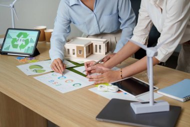İki iş kadını ESG girişimlerinde işbirliği yapıyor, sürdürülebilirlik verilerini analiz ediyor ve çevre dostu çözümleri tartışıyor.