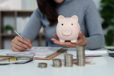 Genç bir kadın, evinde kumbarasını tutarken tasarruf stratejisini analiz ediyor ve mali yetkilendirmeye odaklanıyor..