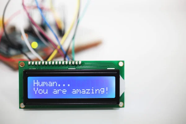 A blue LCD display showing the phrase \'Human you are amazing\' with wires coming from a computer circuit board in the background.