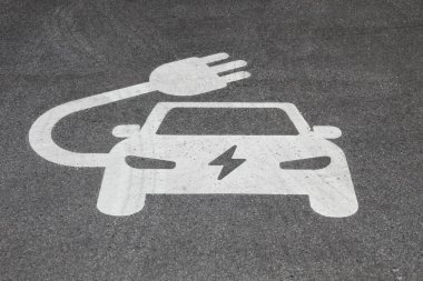 Beyaz elektrikli araba şarj noktası tabelası bir otoparkta koyu gri piste boyanır..