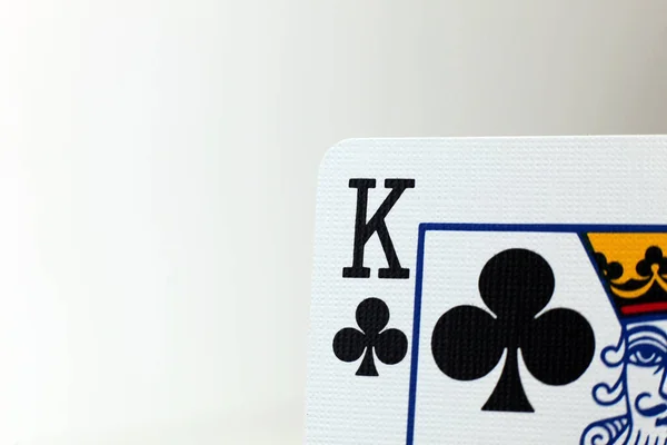A macro photo of the King of Clubs playing card, showing the texture of the card, set against a pale background.