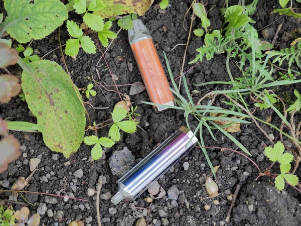 İki elektronik sigara şişesi çalılıkların arasına atıldı. Biri diğerinden daha yaşlı ve kirli görünüyor..