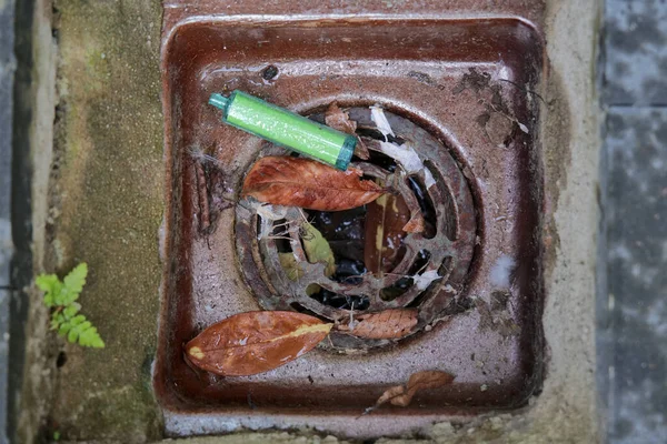 Paslı bir su giderinin üzerine atılmış yeşil bir elektronik sigara kutusu bırakılmış..