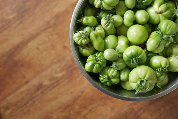 Yeşillik yeşil domates hasadı. Tepeden tırnağa gümüş bir kâse içinde. Odaklanamayan ahşap arka planda. 