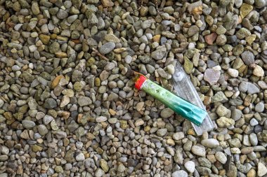 A green neon coloured disposable electronic cigarette vape has been broken and left on some shingle gravel. clipart