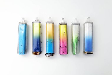 A collection of broken, cracked, and rusty discarded electronic cigarette vapes that have been picked up from roadsides. Shot on a white worktop.