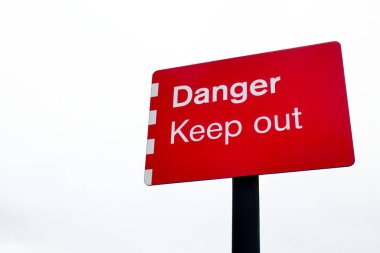 Arkasında beyaz gökyüzü olan ve fotokopi alanı için yeri olan canlı kırmızı bir Tehlike Uzak Kal işareti.