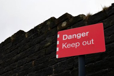 Karanlık uğursuz bir taş duvarın önünde canlı kırmızı bir Tehlike Uzak Kal tabelası. Arkada beyaz bir gökyüzü, fotokopi alanı için yer var..