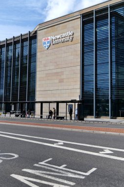 Newcastle, UK 03 27. 2024 Newcastle Üniversitesi Kings Gate binası. Üniversite logosu ve kumtaşı duvarında harfler var. Modern koyu camlı pencerelerin yanında insanlar otobüs durağında bekliyor.