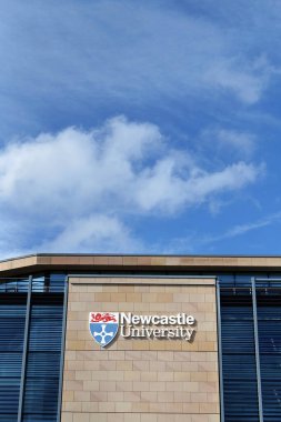 Newcastle, UK 03 27. 2024 Newcastle Üniversitesi Kings Gate binası. Üniversite logosu ve kumtaşı duvarında harfler var. Yanında gökyüzünde kopya alanı olan modern koyu cam pencereler var.