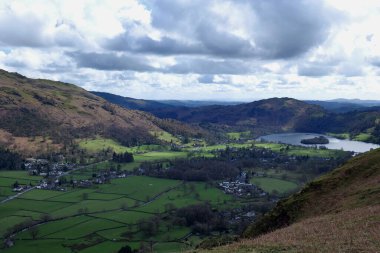 Looking down to the village of Grasmere in Cumbria from Helmcarg. Grassy pastures can be seen between heather covered hills. clipart