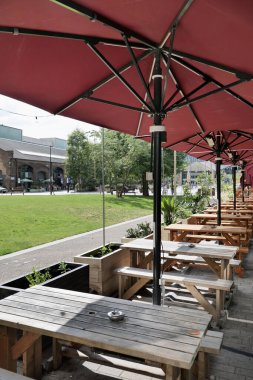 Londra, İngiltere 08: 27 2024 Coals Drop Yard alışveriş merkezi yakınlarında parlak bir yaz gününde kırmızı şemsiyeli ahşap piknik masaları..