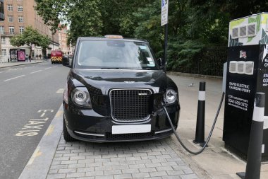 Londra, İngiltere 08: 27 2024 siyah bir Londra taksisi şehirde bir e-taksi hızlı şarj noktasında şarj ediliyor. Ön camdaki plaka ve diğer kimlik bilgileri kaldırıldı.