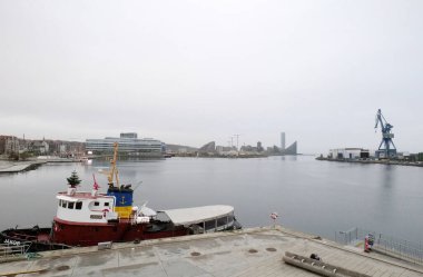 Aarhus, Danimarka 106 2024 Aarhus limanını bulutlu gri bir günde görüyor. Beton bir iskeleye demirlenmiş bir tekne ve ufukta seyrüsefer gemisi görülebilir..