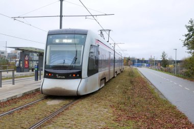 Aarhus, Denmark 11 08 2024 An Aarhus light rail (Aarhus Letbane) electric train travels alongside a cycle lane as it approaches the University Hospital stop. clipart