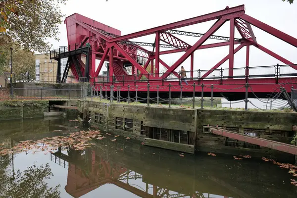 Londra, İngiltere 11: 09 2024 Kırmızı bir scherzer baskülü yuvarlanan kaldırma köprüsü Thames Nehri 'ne açılan kanal havzalarına giriş sağlıyor..
