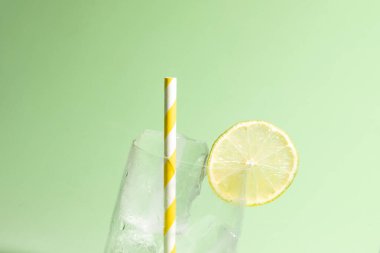 Bir dilim kireç ve çizgili sarı ve beyaz pipetle buz dolu soğuk bir bardak.