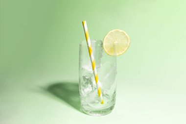 Bir dilim kireç ve çizgili sarı ve beyaz pipetle buz dolu soğuk bir bardak.