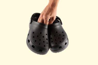 Lastik terlik ya da sandalet tutan erkek el, ayakkabı takımı konsepti, izole edilmiş sarı arka plan. Yüksek kalite fotoğraf