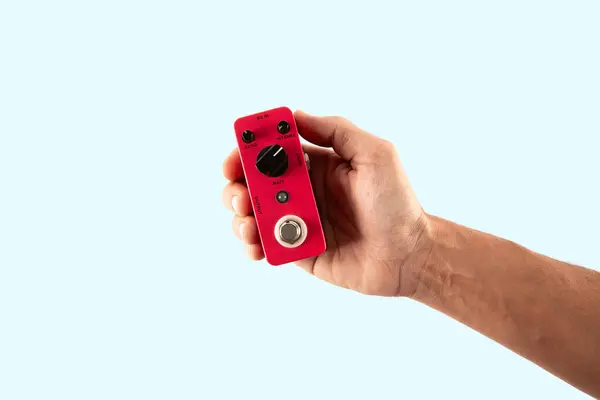 Cyan arka planda izole edilmiş pembe bir gitar efekti pedalı tutan erkek el. Yüksek kalite fotoğraf